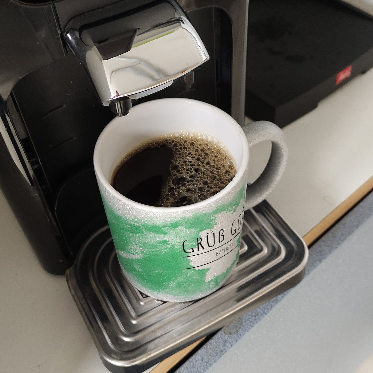 Hallo auf Bayerisch Grüß Gott lustiger Kaffeebecher mit grünem Hintergrund