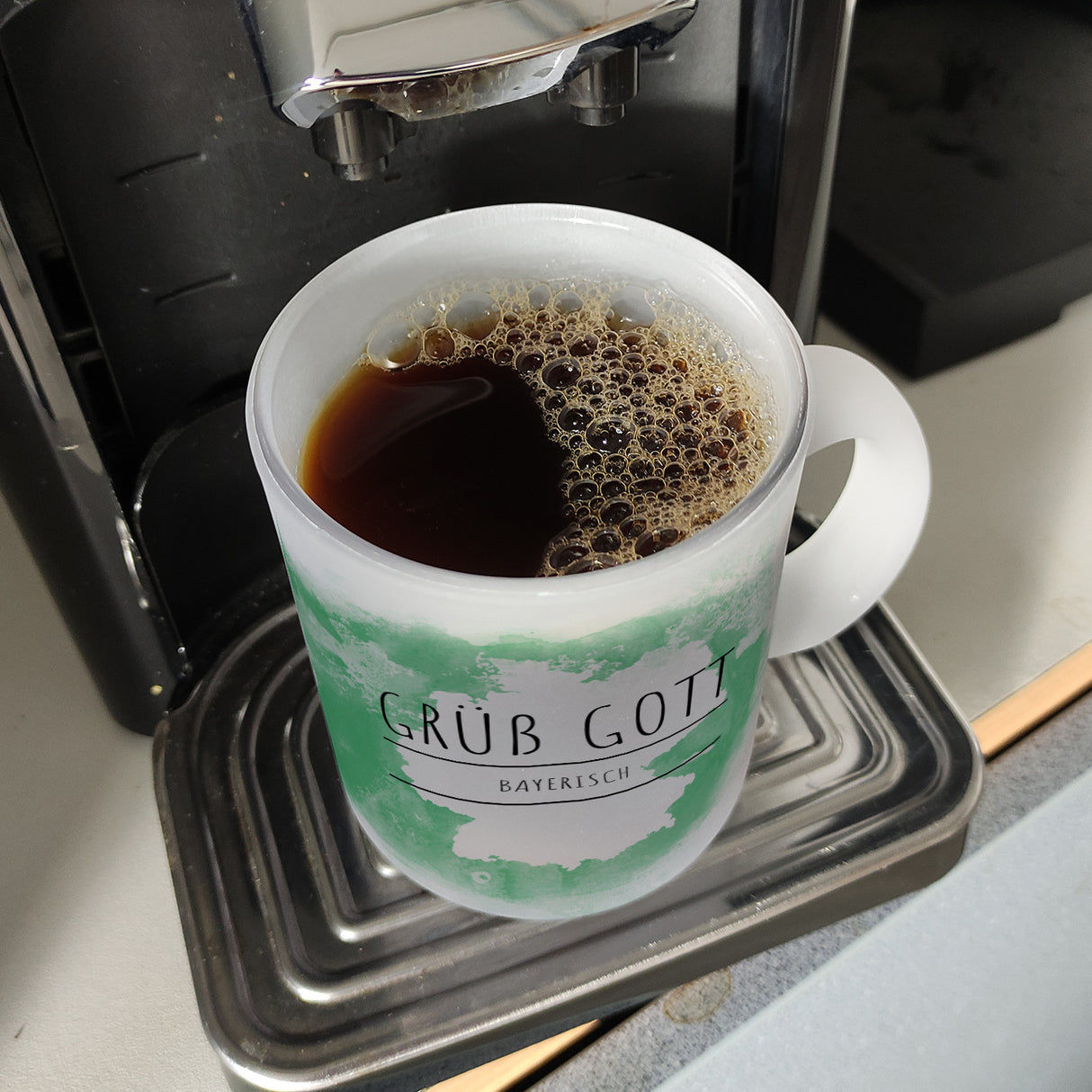 Hallo auf Bayerisch Grüß Gott lustiger Kaffeebecher mit grünem Hintergrund