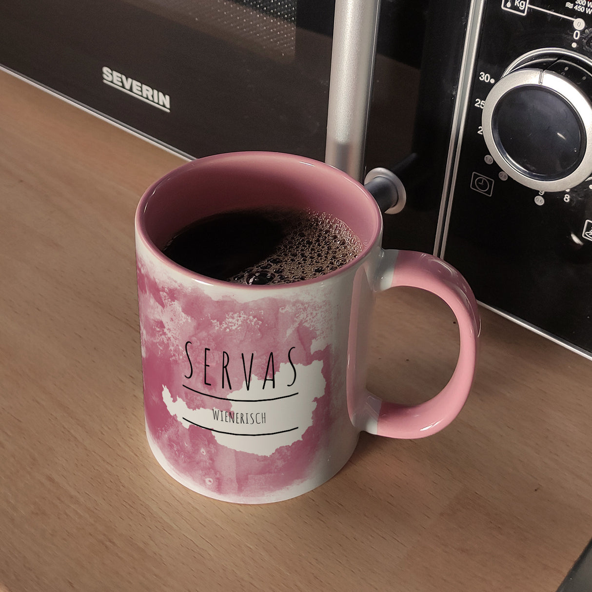 Hallo auf Wienerisch Servas lustiger Kaffeebecher mit rosaem Hintergrund