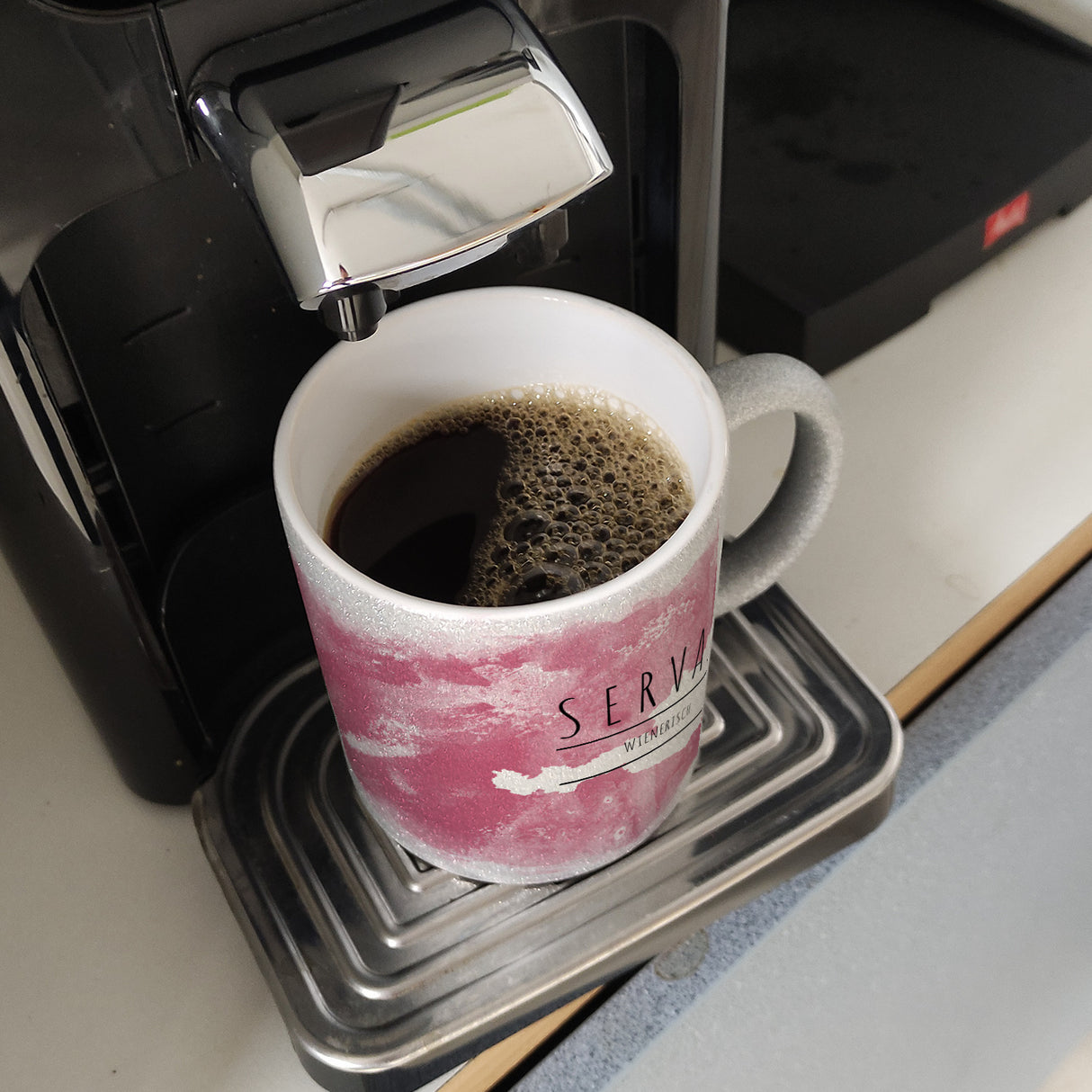 Hallo auf Wienerisch Servas lustiger Kaffeebecher mit rosaem Hintergrund