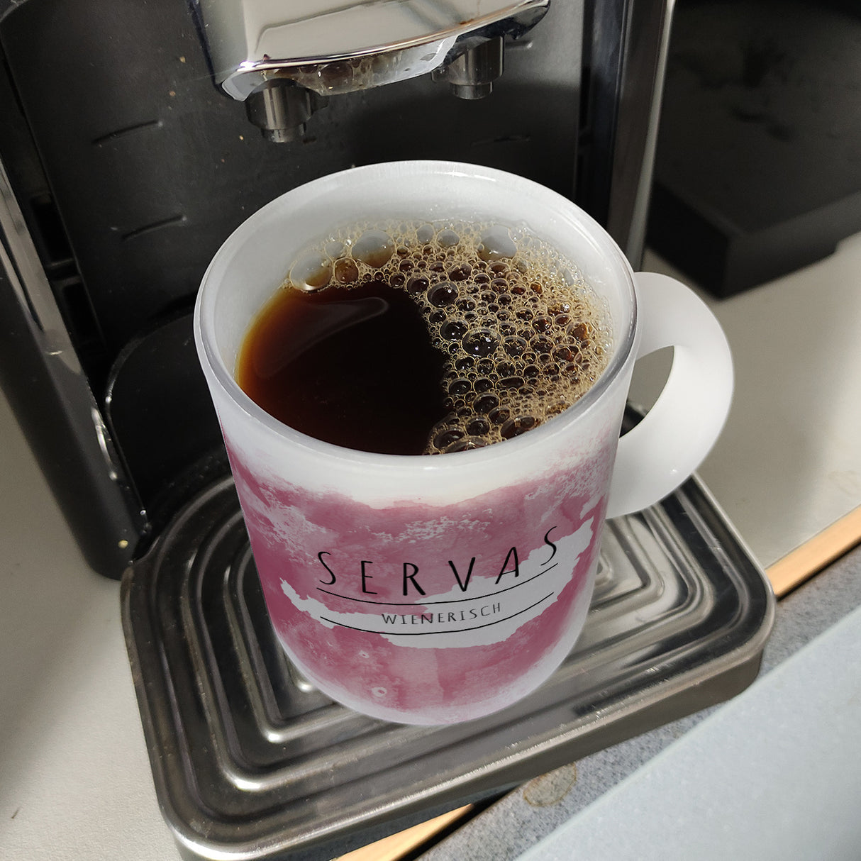 Hallo auf Wienerisch Servas lustiger Kaffeebecher mit rosaem Hintergrund