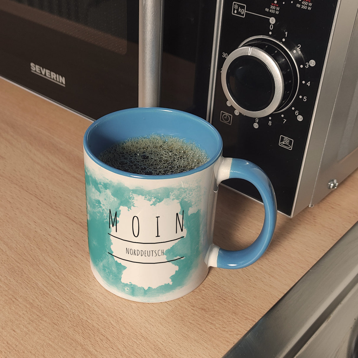 Hallo auf Norddeutsch Moin lustiger Kaffeebecher mit blauem Hintergrund