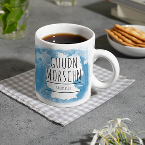 Hallo auf Sächsisch Guudn Morschen lustiger Kaffeebecher mit blauem Hintergrund